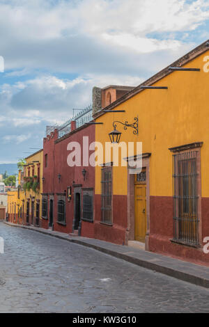 Vieilles maisons colorées avec des détails architecturaux d'une doublure de rue pavée, avec un ciel bleu nuageux, dramatique, à San Miguel de Allende, Mexique Banque D'Images