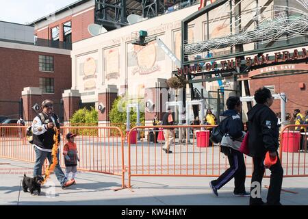 Un homme promène son chien en laisse décorées aux couleurs des géants en direction de O'Doul Gate avant les jours de canicule articles promotionnels d'un match de baseball, un événement annuel dans lequel l'équipe de baseball des Giants de San Francisco permet aux fans d'amener leurs chiens pour un match de saison régulière, à l'extérieur dans le parc d'ATT Chine Quartier Bassin de San Francisco, Californie, le 21 août 2016. Banque D'Images