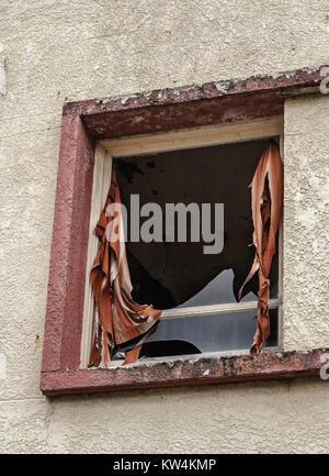 Tattered des rideaux rouges et un peu cassée de verre restent dans un cadre de fenêtre d'un vieux bâtiment abandonné, le stuc, avec des notes d'un vitrail à l'intérieur du plafond. Banque D'Images