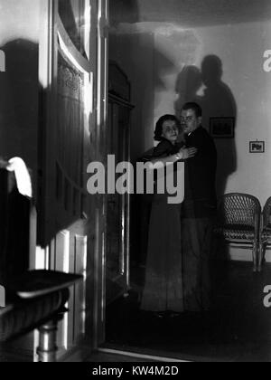 Dans un endroit sombre, très éclairée, un couple danse au milieu de la distance, avec leurs ombres projetées sur le mur derrière eux, Hongrie, 1929. Numérisé à partir d'un processus de gélatine sur plaque de verre, avec quelques dommages présents sur le négatif original. Banque D'Images