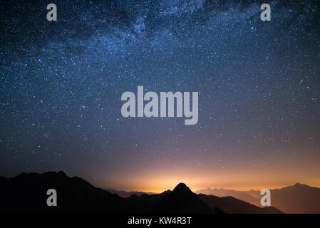 Le merveilleux ciel étoilé sur l'époque de Noël et la majestueuse chaîne de montagnes élevées des Alpes italiennes, avec des villages lumineux ci-dessous. Banque D'Images