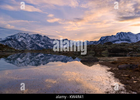 Lac alpin de haute altitude dans un paysage idyllique. Reflet de snowcapped mountain range et panoramique ciel coloré au coucher du soleil. Prise de vue au grand angle pris sur la th Banque D'Images