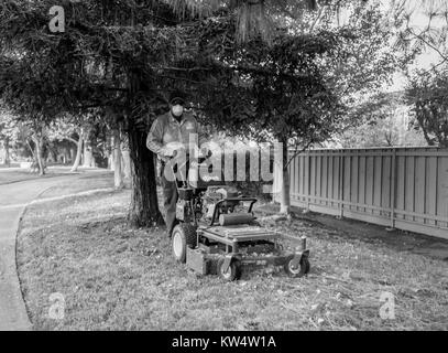 Image en noir et blanc d'un paysagiste chargé de porter un masque antipoussière et debout avec sa tondeuse sur le côté d'une route à Walnut Creek, Californie, le 14 septembre 2016. Banque D'Images