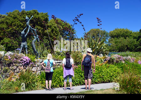 3 Vacanciers à la recherche à la sculpture en bronze de David Wynne de trois enfants jouant dans Tresco Abbey Gardens, Tresco, Îles Scilly, Cornwall. Banque D'Images