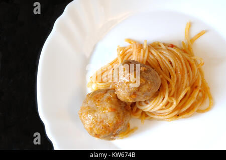 Spaghetti à la sauce tomate et boulettes, recette italienne typique, sur une assiette blanche, fond noir Banque D'Images
