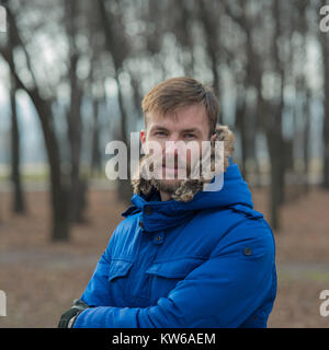 Portrait d'un homme barbu dans les vêtements d'hiver sur un arrière-plan flou d'arbres. Homme barbu souriant. Homme barbu. Banque D'Images