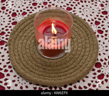 Une bougie rouge dans un bocal en verre sur une plaque de tissu vert assis sur un tapis de table blanc et rouge Banque D'Images