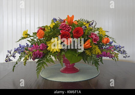 Une pièce maîtresse horizontale colorée, remplie de roses, des lis, des marguerites, mufliers, delphinium et feuillage en cascade sur une table en bois blanc contre. Banque D'Images