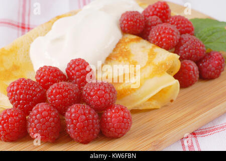 Crêpes avec les framboises fraîches et crème sur planche à découper en bois Banque D'Images