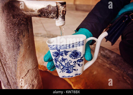 Main dans la main une tasse de remplissage avec de l'eau minérales thérapeutiques lors d'une source chaude naturelle dans la région de Karlovy Vary en hiver, en République Tchèque Banque D'Images