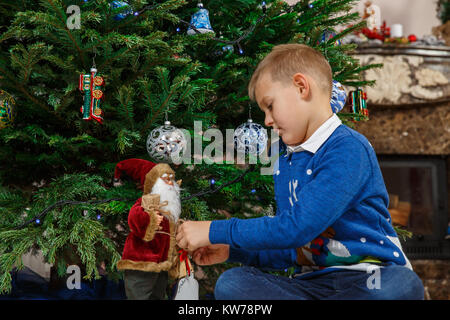 Little Boy decorating Christmas Tree. Enfant heureux Noël avec Santa doll. Maison de vacances d'hiver et vacances. Christmasmas partie célébration. Banque D'Images