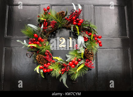 Gros plan de la couronne de Noël sur la porte d'entrée de la maison de ville géorgienne, Edinburgh New Town, Écosse, Royaume-Uni, avec le numéro en laiton 21 sur la porte à panneaux noirs Banque D'Images