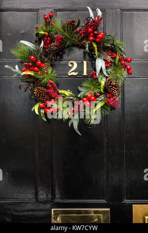 Gros plan de la couronne de Noël sur la porte d'entrée de la maison de ville géorgienne, Edinburgh New Town, Écosse, Royaume-Uni, avec le numéro en laiton 21 sur la porte à panneaux noirs Banque D'Images