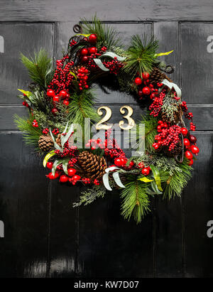 Couronne décorative de Noël sur la porte d'entrée de la maison de ville géorgienne, Edinburgh New Town, Écosse, Royaume-Uni, avec le numéro de laiton 23 sur la porte à panneaux noirs Banque D'Images