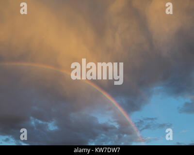 Demi-cercle de différentes couleurs d'un arc-en-ciel lumineux dans un ciel nuageux gris, éclairé par les rayons du soleil. Banque D'Images