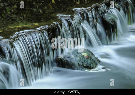 La rivière Dove circulant sur un petit barrage de la vallée boisée de Beresford Dale dans le parc national de Peak District, England, UK Banque D'Images