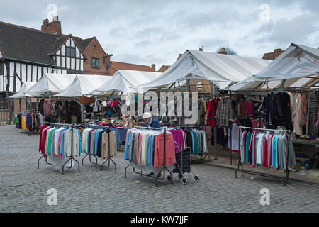 Vieille dame en place du marché historique, examine les cavaliers hanging on rails par vêtements, les étals de marché - Shambles York, North Yorkshire, Angleterre, Royaume-Uni. Banque D'Images