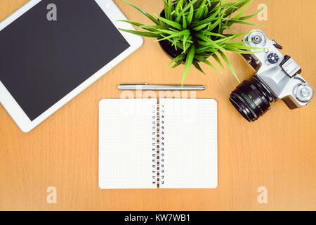 Concept de créativité en milieu de travail - Vue de dessus de l'appareil photo reflex rétro vert, fleur, tablette numérique et bloc-notes avec stylo sur un bureau en bois. Banque D'Images