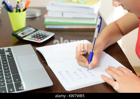 Jeune écolière est en train de faire un travail avec les mathématiques à côté d'un ordinateur portable, une calculatrice et des livres sur son bureau dans sa chambre Banque D'Images