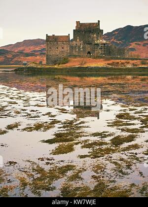 Marées dans le lac au château Eilean Donan, Ecosse. Le célèbre pont de pierre sur les restes de l'eau avec des touffes d'algues de l'eau. La lumière faible Banque D'Images