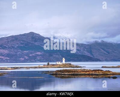 Iasle Ornsay phare construit sur une petite île située sur le trajet. Faible niveau d'eau. Snowy Mountain peaks cachés dans nuageux backgroun Banque D'Images