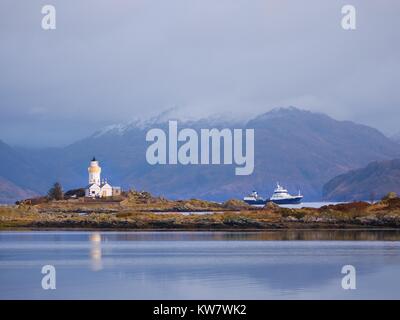 Phare sur Isle Ornsay, de la rive sud de l'île de Skye, en Ecosse. Navire de commerce à Rocky island, montagnes en arrière-plan Banque D'Images