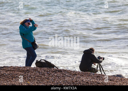 Un photographe, s'assoit et prend une photo des rochers et des vagues sur la plage d'Hastings avec son partenaire d'ennuie en attente, East Sussex Banque D'Images