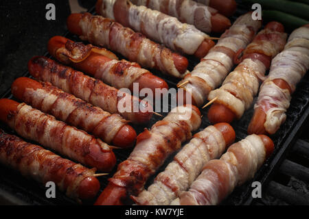 Close-up de quatorze juteuse bacon-enveloppé de hot-dogs cuits sur une grille, dans un arrangement diagonal pendant un camp-out ou pique-nique en plein air. Banque D'Images