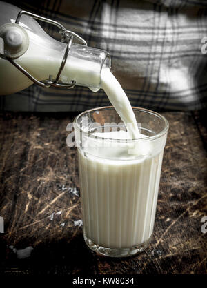 Femme verse du lait de vache frais dans un verre. Sur une table en bois. Banque D'Images