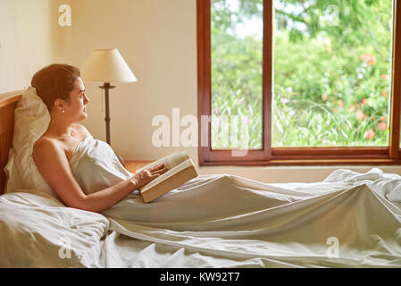 Livre de lecture dans la chambre avec grande fenêtre. Jeune fille au livre Banque D'Images