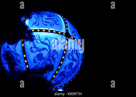 Grande boule de Noël bleue illuminée la nuit. Motif fleuri vintage. Suspendu à un arbre de Noël extérieur Banque D'Images