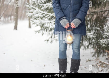 Woman holding lanterne sur le chemin boisé tandis qu'il neige à l'extérieur Banque D'Images