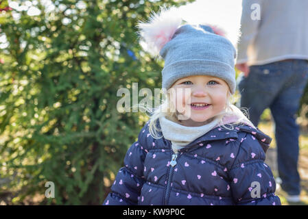 Smiling little girl in winter coat à la recherche d'un arbre de Noël en famille Banque D'Images