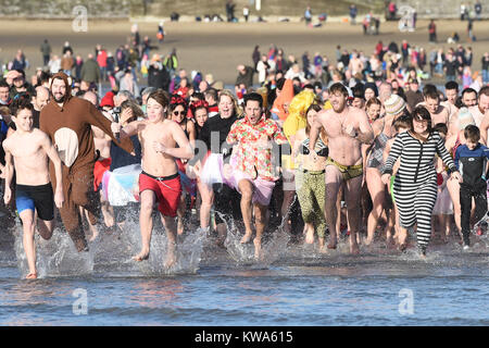 Rencontrez des nageurs dans la mer à l'île de Barry Nouvelle Année Jour nager à Whitmore Bay, dans la vallée de Glamorgan, Pays de Galles, au cours de la 34e édition du Nouvel An nager, qui à l'origine commencé lorsque cinq membres de l'Jacksons Bay Lifeguard Club a décidé de se débarrasser de leur gueule avec quelques brasses, submergeant complètement par eux-mêmes trois fois. Banque D'Images