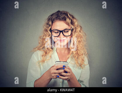 Jeune femme dans la navigation contenu lunettes smartphone sur fond gris. Banque D'Images
