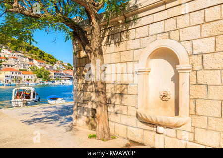 Mur de briques avec un robinet d'eau dans Povlja port avec bateaux de pêche, île de Brac, Croatie Banque D'Images