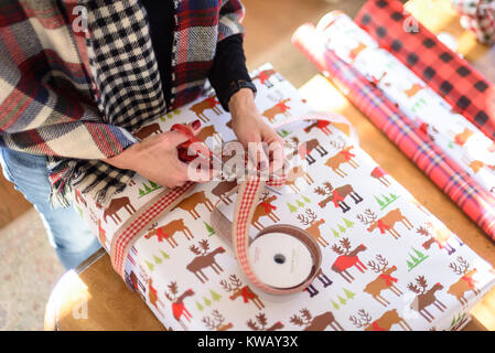 Closeup of woman wrapping Christmas Gift à table avec les ciseaux et les rouleaux de papier Banque D'Images