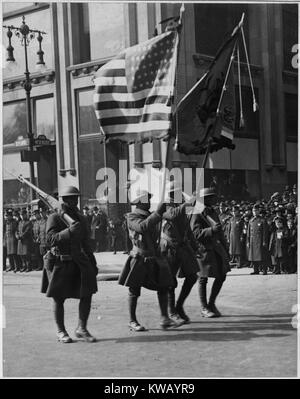 Quatre hommes africains-américains en uniforme à pied en formation dans la rue portant des drapeaux et des armes à feu lors d'un défilé pour la célèbre 369e Infantry, à son retour de France, New York, New York, 1919. L'image de courtoisie des Archives nationales. Banque D'Images