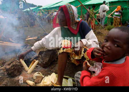 Cyuve, camp de réfugiés du Rwanda, de l'éruption du volcan Nyriragongo le 18 Jan 2002 dans les environs de Goma en RDC. Ici une mère cuisiniers certains maïs doux pendant qu'en arrière-plan les réfugiés construire des abris temporaires. Banque D'Images