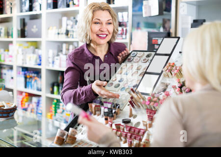 Smiling mature femme positive vendeur près de display avec les cosmétiques au magasin de beauté Banque D'Images