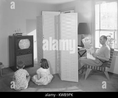 Père lisant le journal, tandis que deux enfants d'anticiper le début de la télévision. Dans un appartement de la ville de New York, le téléviseur affiche un modèle de test avant de commencer sa journée de radiodiffusion. Le 12 juillet 1950. (BSLOC   162 13 2014) Banque D'Images