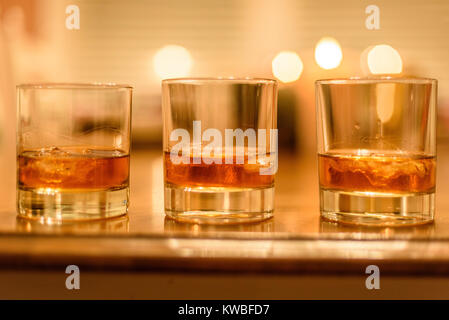 Gros plan du bourbon whiskey verres avec de la glace se sont alignées sur la table en bois avec des bougies en arrière-plan Banque D'Images