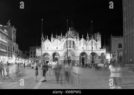 Blurry motion image de personnes à pied à la place Saint-Marc (Piazza San Marco) dans la nuit avec un célèbre monument basilique dans l'arrière-plan. Banque D'Images