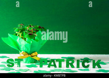 Clover pot enveloppé dans du papier vert et doré et ruban arc et les paroles St Patrick écrit en lettres en bois vert, entouré par du papier trèfle. Banque D'Images