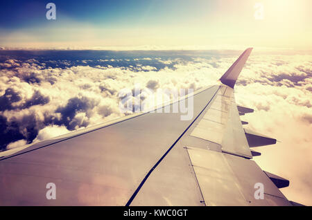 Une aile d'avion au-dessus des nuages au coucher du soleil vu à travers une fenêtre d'un aéronef, couleur tonique travel concept photo. Banque D'Images