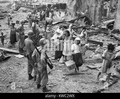 Les femmes et les enfants à chercher comment s'y prendre les pieds nus sur l'épave de l'Manille, ca. 23 février, 1945. Il vient d'arriver sur le lieu de l'Amérique sûr par rapport à côté de la rivière Pasig, après s'être échappé de la ville fortifiée attaquée amèrement (Intramuos) au sud. Le catholique sœur porte un enfant né de mère trois jours avant dans la ville fortifiée au milieu des combats. World War 2 (BSLOC   2015 13 126) Banque D'Images