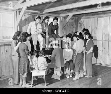 Les internés Japonais-américain réunis autour du piano à Manzanar War Relocation Center. La "Communauté chanter Session" est fréquenté surtout par les jeunes femmes, avec un jeune homme et de deux enfants. Le 2 mai 1942. (BSLOC   2015 13 104) Banque D'Images