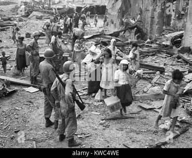 Les femmes et les enfants à chercher comment s'y prendre les pieds nus sur l'épave de l'Manille, ca. 23 février, 1945. Il vient d'arriver sur le lieu de l'Amérique sûr par rapport à côté de la rivière Pasig, après s'être échappé de la ville fortifiée attaquée amèrement (Intramuos) au sud. Le catholique sœur porte un enfant né de mère trois jours avant dans la ville fortifiée au milieu des combats. World War 2 (BSLOC   2015 13 126) Banque D'Images