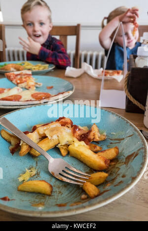 Une plaque à moitié mangé des chips au fromage avec du ketchup sur une table devant des enfants de manger des aliments. Banque D'Images