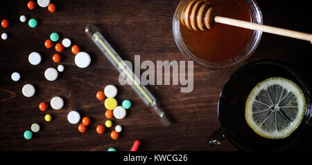 Médicaments et pilules sur une table en bois. Divers moyens pour prévenir les rhumes. Thé au citron et de miel. Tasse en verre avec plateau tranche de citron et un pot de miel. Banque D'Images